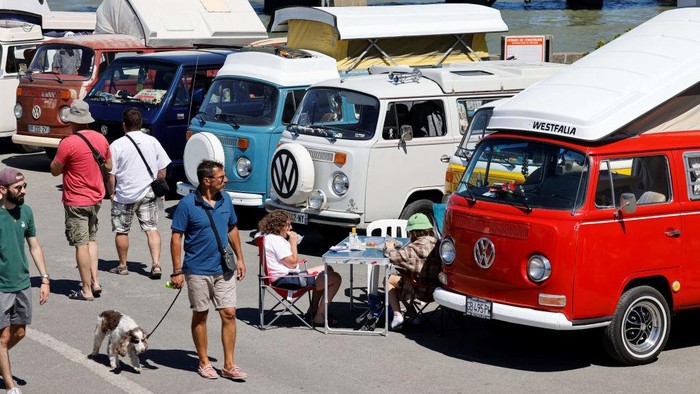 Ratusan VW Kombi Mejeng di Pantai Prancis, Hadirkan Nuansa Nostalgia Pedestrians walk past vintage Volkswagen Kombi (VW Combi) vans during the third Fromentine Vintage Cup in Fromentine, western France, on August 7, 2022. - The Fromentine Cup is an annual gathering vintage van, Volkswagen Kombi trucks, and surfboarding enthusiasts, on the western coast of France. (Photo by Ludovic MARIN / AFP) (Photo by LUDOVIC MARIN/AFP via Getty Images)