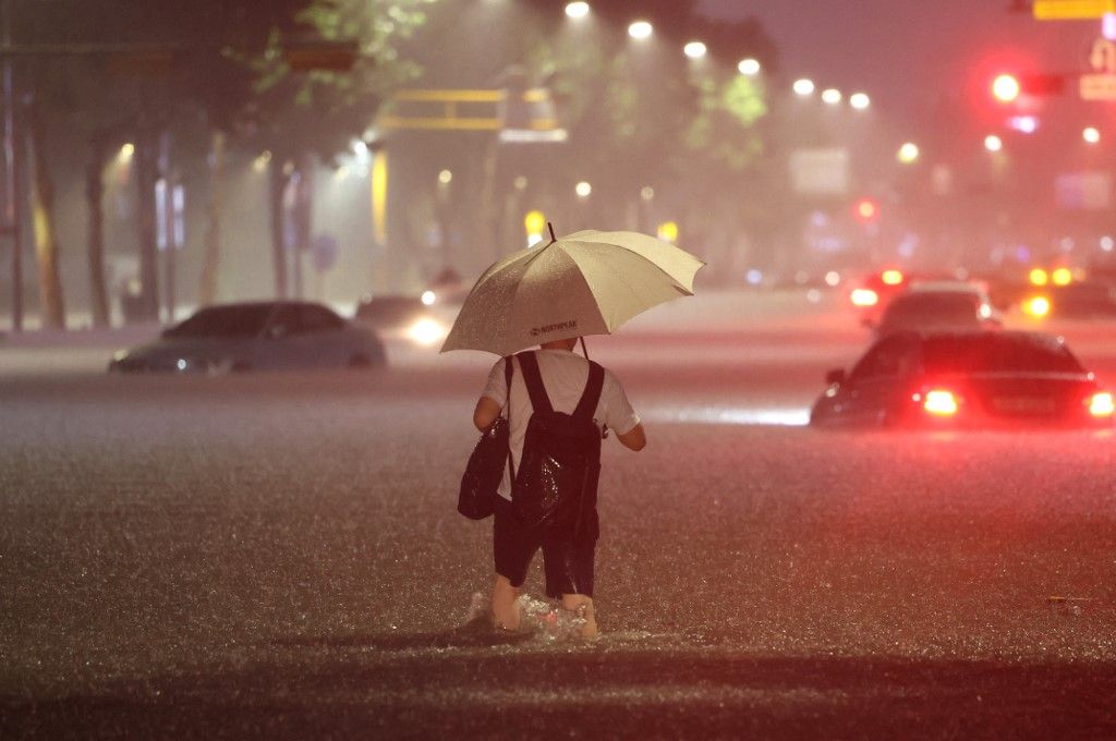 A man wades alongside submerged cars in a street during heavy rainfall in the Gangnam district of Seoul on August 8, 2022. (Photo by YONHAP / AFP) / - South Korea OUT / NO ARCHIVES -  RESTRICTED TO SUBSCRIPTION USE