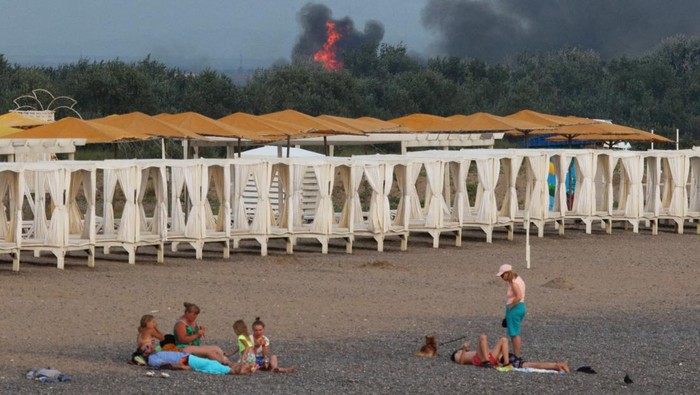 People rest on a beach as smoke and flames rise after explosions at a Russian military airbase, in Novofedorivka, Crimea August 9, 2022. REUTERS/Stringer     TPX IMAGES OF THE DAY