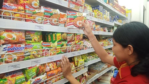 Salah satu karyawati di salah satu minimarket di Denpasar sedang merapikan mie instan di etalase