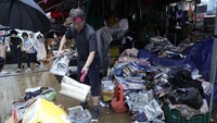 Seorang pedagang tengah merapikan barang dagangannya yang tersapu banjir.