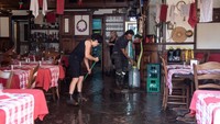 Pemilik salah satu restoran membersihkan lantai dan juga barang- barang yang terkena lumpur dan puing-puing setelah banjir parah.
