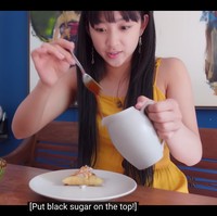 Lewat vlognya, Dita Karang juga memperkenalkan kue lapis sebagai dessert Indonesia kepada penggemar mancanegara. Dia memakai dress berwarna kuning dan anting panjang bertuliskan aksara Jawa. Foto: dok. YouTube Secret Number