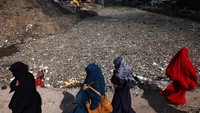 Sejumlah wanita berjalan di sepanjang jembatan di atas kanal yang penuh sampah. Keberadaan sampah ini akibat dari sistem pengolahan sampah yang belum maksimal. 