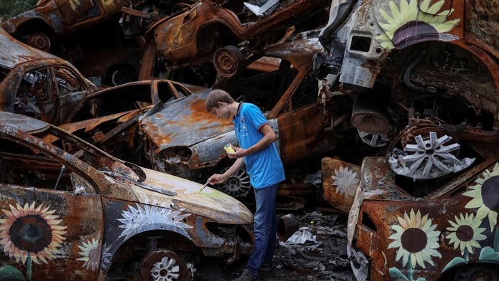 A Ukrainian artist Viacheslav Rybka paints a car destroyed during Russia's attack on Ukraine and then collected from different places in the town of Irpin in Kyiv region, Ukraine August 10, 2022. REUTERS/Gleb Garanich     TPX IMAGES OF THE DAY