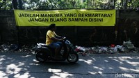 Warga melintas di depan spanduk larangan membuang sampah. Spanduk tersebut terlihat tak berguna karena tumpukan sampah masih banyak ditemui di tempat ini.