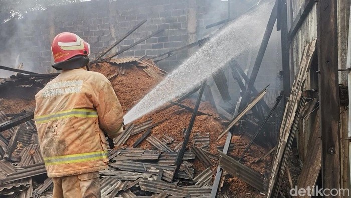 Petugas melakukan pembasahan gudang serbuk kayu terbakar di Gresik