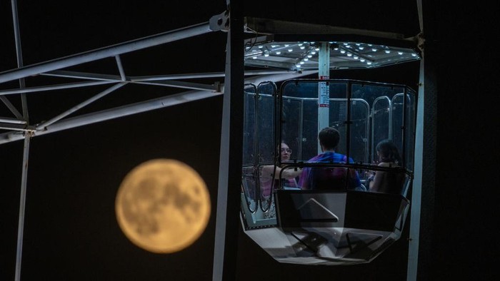 BRISTOL, ENGLAND - AUGUST 11: The August full moon known as the 'Sturgeon Moon' rises behind the ferris wheel at Bristol International Balloon Fiesta at Ashton Court Estate, on August 11, 2022 in Bristol, England. From the event's small beginning in 1979, the Fiesta has grown into what has become Europe's largest annual hot air balloon festival. The Bristol International Balloon Fiesta is a charity, run by a committee, and remains free of charge to the public. It attracts over 100 hot-air balloons and 500,000 visitors over the four days of the event. (Photo by Finnbarr Webster/Getty Images)