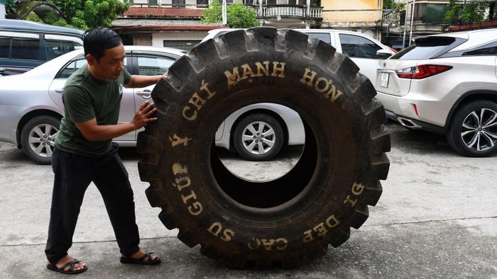 This photo taken on July 8, 2022 shows Nguyen Tien Cuong pushing a truck tyre outside a workshop in Hanoi, before it's transformed into rubber tyres. - Made from recycled military truck or aircraft tyres, Vietnam's hand-made rubber sandals, the famously rugged footwear of the Viet Cong, have travelled vast distances over the decades. - TO GO WITH AFP STORY Vietnam-history-lifestyle-sandals by Tran Thi Minh Ha (Photo by Nhac NGUYEN / AFP) / TO GO WITH AFP STORY Vietnam-history-lifestyle-sandals by Tran Thi Minh Ha (Photo by NHAC NGUYEN/AFP via Getty Images)