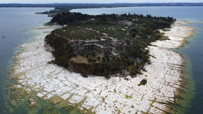 Potret Danau Terbesar di Italia Airnya Menyusut Akibat Kekeringan Parah A view of the peninsula of Sirmione, on Garda lake, Italy, Friday, Aug. 12, 2022. Lake Garda water level has dropped critically following severe drought resulting in rocks to emerge around the Sirmione Peninsula. (AP Photo/Antonio Calanni)