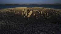 Amalie Garcia (54) berdiri di samping The Dolmen of Guadalperal, di dasar waduk Valdecanas di El Gordo, Spanyol barat, Sabtu, (13/8/2022). Monumen tersebut merupakan situs kuno pada era megalitikum. The Dolmen of Guadalperal terlihat karena air waduk surut lantaran kekeringan dan gelombang panas.
