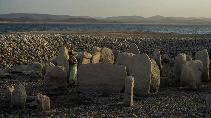 Amalie Garcia, 54, stands next to The Dolmen of Guadalperal, a megalithic monument that emerged due to drought at the Valdecanas reservoir in El Gordo, western Spain, Saturday, Aug. 13, 2022. In the wake of three heatwaves and little rain in sight, Spains reservoirs are getting emptier by the week, and not just in traditionally more arid southern part of the country. Spains drought began early in the year after the country suffered its second driest winter in more than 60 years, according to the government. (AP Photo/Manu Fernandez)