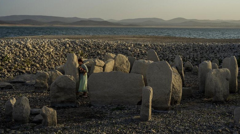Air Waduk Surut, Stonehenge Spanyol Muncul Lagi Amalie Garcia, 54, stands next to The Dolmen of Guadalperal, a megalithic monument that emerged due to drought at the Valdecanas reservoir in El Gordo, western Spain, Saturday, Aug. 13, 2022. In the wake of three heatwaves and little rain in sight, Spains reservoirs are getting emptier by the week, and not just in traditionally more arid southern part of the country. Spains drought began early in the year after the country suffered its second driest winter in more than 60 years, according to the government. (AP Photo/Manu Fernandez)