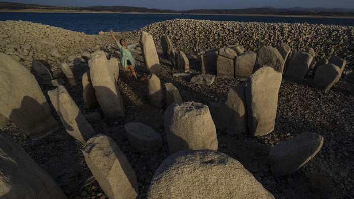 Amalie Garcia, 54, stands next to The Dolmen of Guadalperal, a megalithic monument that emerged due to drought at the Valdecanas reservoir in El Gordo, western Spain, Saturday, Aug. 13, 2022. In the wake of three heatwaves and little rain in sight, Spain's reservoirs are getting emptier by the week, and not just in traditionally more arid southern part of the country. Spain's drought began early in the year after the country suffered its second driest winter in more than 60 years, according to the government. (AP Photo/Manu Fernandez)