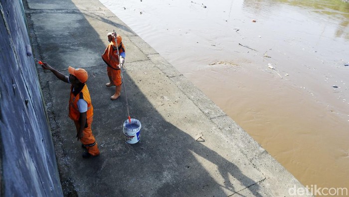 Dua petugas melakukan perawatan dengan membersihkan dinding turap Kali Ciliwung yang berada di pemukiman Jatinegara, Jakarta, Selasa (16/08/2022). Dinding juga dicat kembali oleh petugas.