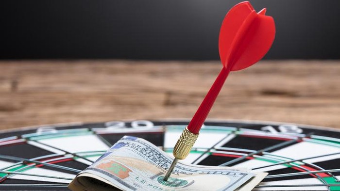 Closeup of arrow in papernotes on dartboard at table against black background