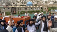 Pelayat membawa peti jenazah sebelum dikebumikan. Di belakangnya, terdapat masjid lokasi ledakan bom yang menewaskan 10 orang. Terlihat para pria memelihara jenggot seperti yang diwajibkan oleh rezim Taliban.