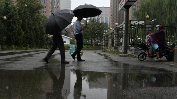 Residents walk with umbrellas near a puddle during a rainy day in Beijing, Thursday, Aug. 18, 2022. Some were killed with others missing after a flash flood in western China Thursday, as China faces both summer rains and severe heat and drought in different parts of the country. (AP Photo/Ng Han Guan)