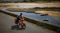 Pesepeda melintas di samping Sungai Loire dengan debit air menyusut drastis. Suhu panas ekstrem yang terjadi sejak Juli membuat Prancis mengalami kekeringan.