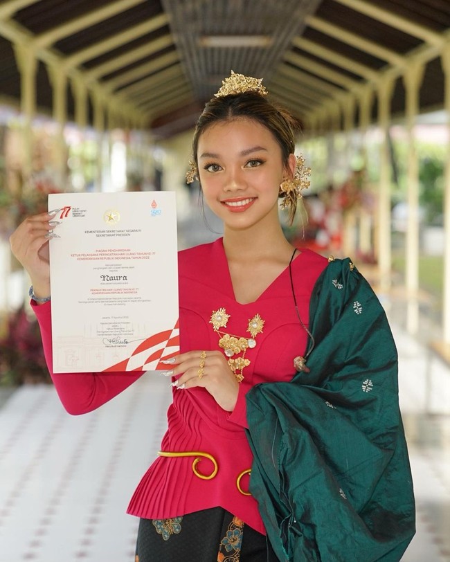 Untuk riasan, mantan pacar Devano Danendra tersebut menonjolkan makeup mata dengan aksentuasi eyeshadow emas. Ia juga menerapkan lipstik bernuansa oranye yang segar dan serasi dengan busana. Foto: Instagram Naura Ayu