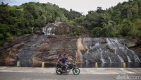 Pengendara motor melintas di depan Air Terjun Temburun di Pulau Siantan, Kabupaten Kepulauan Anambas, Kepulauan Riau, Selasa (2/8/2022). Kepulauan Anambas menyimpan beragam destinasi wisata yang menarik untuk dikunjungi. Tidak heran bila kabupaten termuda di Provinsi Kepulauan Riau ini kerap dijuluki surga kecil di perbatasan Indonesia.  