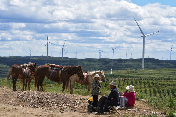 Beachgoers take cover in the shade near wind turbines along the coast of Pingtan in Southern China's Fujian province on Aug. 6, 2022. The world's two biggest emitters of greenhouse gases are sparring on Twitter over climate policy, with China asking if the U.S. can deliver on the landmark climate legislation signed into law by President Joe Biden this week. (AP Photo/Ng Han Guan)