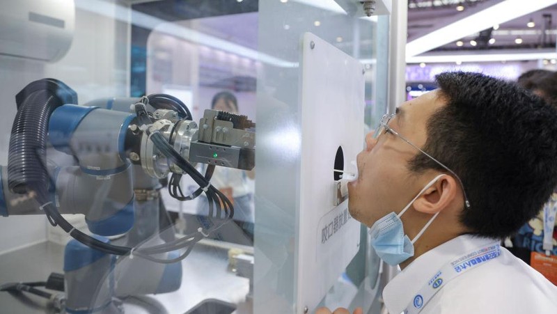 BEIJING, CHINA - AUGUST 18: A staff member takes part in a demonstration of a robot arm collecting swab samples for coronavirus disease (COVID-19) detection during the 2022 World Robot Conference at Beijing Etrong International Exhibition on August 18, 2022 in Beijing, China. The 2022 World Robot Conference kicked off on Thursday in Beijing. (Photo by Lintao Zhang/Getty Images)
