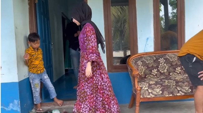 Rumah itu berdinding batako dan tak dihaluskan. Hanya ada cat warna biru yang sudah mulai usang. Ada dua kursi di depan rumahnya. (Foto: YouTube/Mambruut Official)