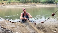 Seorang nelayan mengambil ikan yang terperangkap saat air sungai Rhine menyusut akibat kekeringan di Giesbeek, Belanda, Rabu, (17/8/2022).