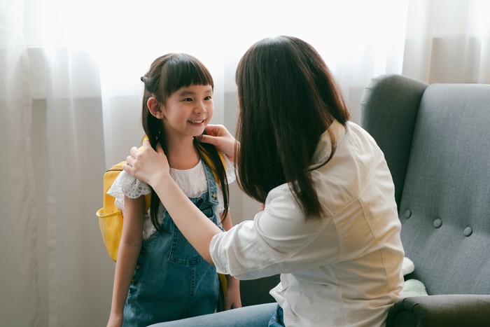 Asian mother help her daughter wearing school bag to prepare go to school.