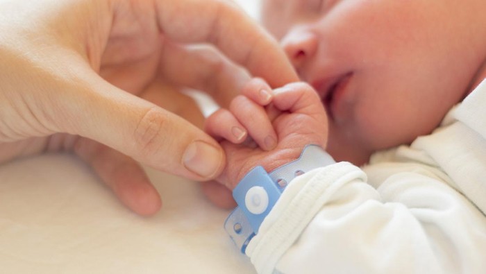 Newborn baby boy sleeping in his crib, his mothers hand holding his little hand.