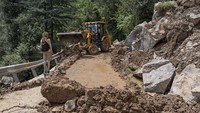 Seorang warga menunggu alat berat yang sedang menyingkirkan timbunan longsor yang menutupi jalan di Dharmsala, Himachal Pradesh, India. (Ashwini Bhatia/AP Photo).