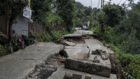 Seorang pria dan wanita duduk di sebelah jalan, yang sebagian ambruk akibat hujan lebat di Dharmsala, negara bagian Himachal Pradesh, India, Minggu, (21/8/2022) (Ashwini Bhatia/AP Photo).