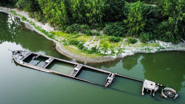 Bentuk Kapal Tongkang Tahun 1943 yang Muncul di Sungai Po Italia Gualtieri, Reggio Emilia, Internati Island, The '' Zibello '' barge. It was sunk during the Second World War by the Germans in 1943 and totally re-emerged due to the worst drought since the seventies which is affecting the Po river and the entire Po valley. 55 meters long and with a capacity of 6 thousand quintals, it was built in the Giudecca shipyard in Venice with metal donated by Austria as a war debt. It was used for the transport of agricultural products, coal and boulders for the construction of infrastructures. (Photo by: Nicola Marfisi/AGF/Universal Images Group via Getty Images)