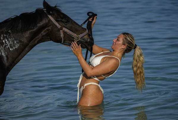 Turis wanita yang senang bermain dengan kuda di Laut Karibia.