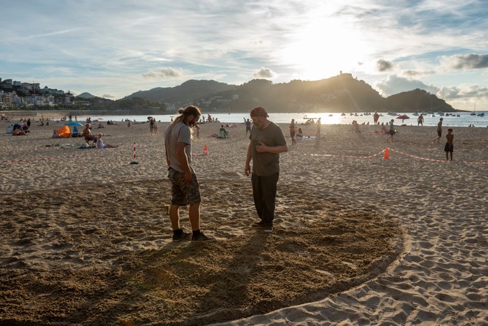 SAN SEBASTIAN, SPAIN - AUGUST 22: Land Art artists Jon Foreman (L) and James Brunt (R) look at five meter diameter symbol of the House Targaryen they created using stones on La Concha beach to promote the 