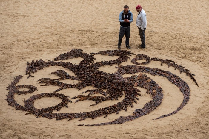Simbol 'Naga Berbatu' Muncul di Tepi Pantai, Promosikan House of the Dragon SAN SEBASTIAN, SPAIN - AUGUST 22: Land Art artists Jon Foreman (L) and James Brunt (R) look at five meter diameter symbol of the House Targaryen they created using stones on La Concha beach to promote the