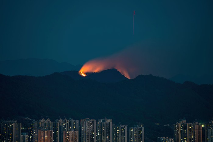 1417559910 CHONGQING, CHINA - AUGUST 23: Smoke and flames rise from a mountain during a wildfire in Banan district on August 23, 2022 in Chongqing, China. The wildfire that broke out last Sunday afternoon has been brought under control by firefighters in Chongqing. (Photo by VCG/VCG via Getty Images)
