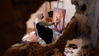 Seniman Palestina melukis di rumah almarhum Duniana Al-Amour yang rusak akibat perang, Selasa (23/8).