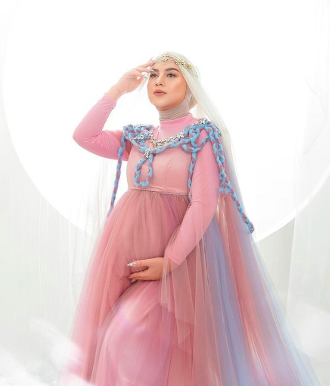 Dalan foto maternity, Irish Bella mengenakan dress pink. Di bagian bawahnya menjuntai bahan tulle pink gradasi warna biru. Foto: dok. Instagram/@_irishbella_