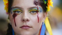 Lukisan wajah pada perempuan ini terlihat nyata, menggambarkan lobang peluru dan air mata darah saat beraksi untuk memperingati Hari Kemerdekaan Ukraina, di Berlin, Jerman, Kamis (24/8/2022). (AP Photo/Markus Schreiber)