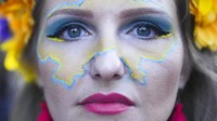 Peta negara Ukraina dilukis di wajah perempuan saat beraksi. Sudah 6 bulan Rusia menggempur kota-kota di Ukraina dan belum ada tanda-tanda selesai.  (AP Photo/Markus Schreiber)
