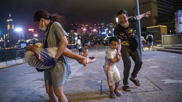 People brave strong wind on the promenade of Victoria Habour as tropical cyclone Ma-on approaches Hong Kong, Wednesday, Aug. 24, 2022. Tropical Storm Ma-on was gaining strength as it headed for Hong Kong and other parts of southeastern China on Wednesday after displacing thousands in the Philippines. (AP Photo/Anthony Kwan)