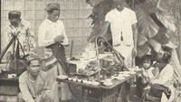 Potret lawas penjual makanan ini diambil di Batavia sekitar tahun 1915. Terlihat seorang penjual sedang melayani kopi untuk pembeli yang mengitari pikulannya. Foto: Instagram @potret.sejarahindonesia/KITLV Leiden