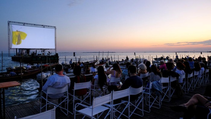 Unik, Begini Sensasi Nonton di Bioskop Terapung Italia People on boats attend a movie screening at a float-in cinema during the 'Floating Cinema β Unknown Waters' event, taking place on the waters of the Venetian lagoon, in Venice, Italy. August 25, 2022. REUTERS/Manuel Silvestri