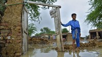 Seorang anak berdiri di depan rumahnya yang rusak akibat diterjang banjir.