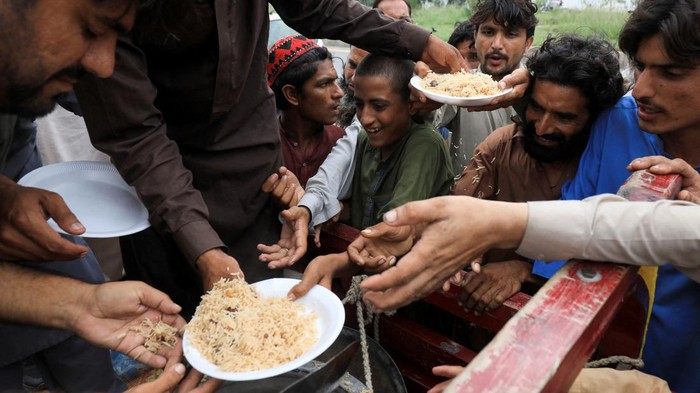 Darurat! 30 Juta Orang Terdampak Banjir di Pakistan Flood victims receive boiled rice from relief workers, after taking refuge on a motorway, following rains and floods during the monsoon season in Charsadda, Pakistan August 27, 2022. REUTERS/Fayaz Aziz