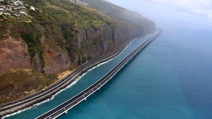 Jalanan Termahal di Prancis Ini Membentang di Tebing Vulkanik This aerial view taken on August 28, 2022, shows vehicles travelling on the 'New Coastal Road' 'Nouvelle Route du Littoral (NRL)' near Saint-Denis La Reunion on the French Indian Ocean Island of Reunion, after it was partially opened - reportedly as Frances most expensive road project. - The coastal viaduct section forms a 5.4km-long section of the 12.5km highway which links the two main cities of Reunion Island, Saint-Denis and La Possession. (Photo by Richard BOUHET / AFP) (Photo by RICHARD BOUHET/AFP via Getty Images)