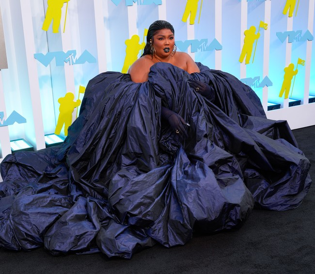 Lizzo sebenarnya bukan tipikal wanita yang takut memamerkan bentuk tubuhnya. Namun di karpet hitam MTV VMA 2022, ia tetap sukses tampil memukau dengan menghadirkan drama dalam balutan gaun megar biru gelap dari Jean Paul Gaultier yang dirancang oleh Glenn Martens. Lipstik dan sarung tangan senada, serta padanan anting statement dan rambut wet-look, kian menyempurnakan gaya pelantun About Damn Time itu. Foto: WireImage/Gotham