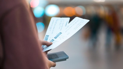 A young girl is going on a trip, holds plane tickets in her hands and goes to check-in, boarding a flight, close-up view of a boarding pass on a blurred background.
